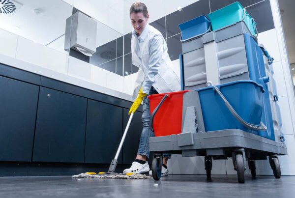 janitorial business insurance Female Janitor Mopping the Floor of a Restroom With Cleaning Cart Focus and View of Sinks in the Background