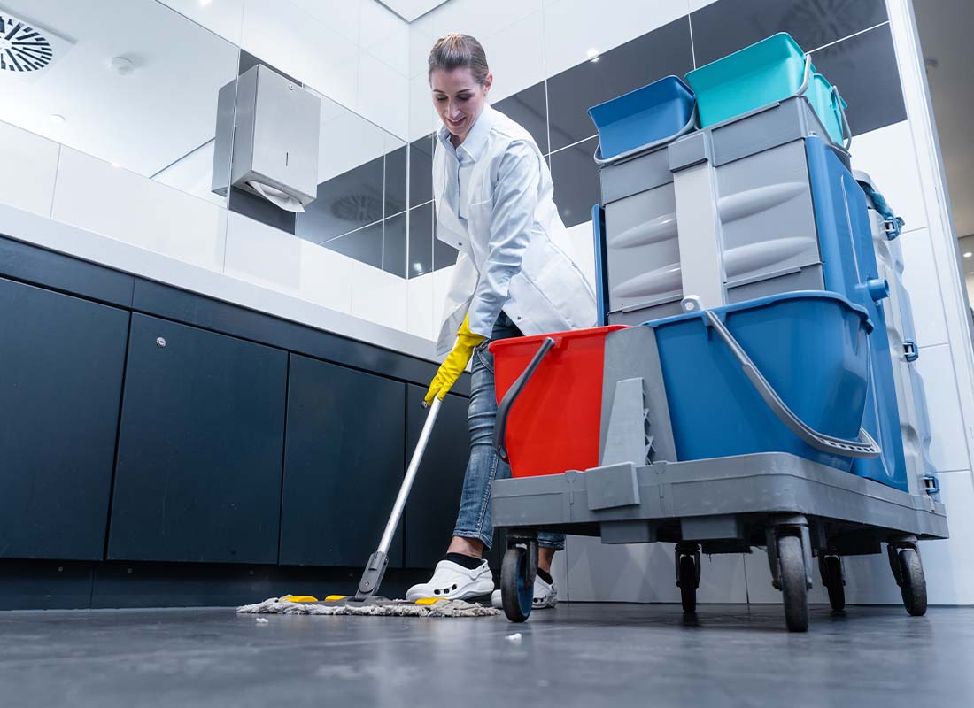janitorial business insurance Female Janitor Mopping the Floor of a Restroom With Cleaning Cart Focus and View of Sinks in the Background